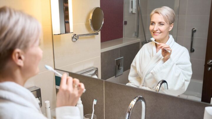 A woman brushing teeth in a bright, modern bathroom.