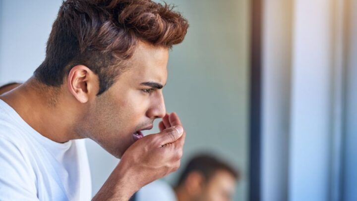 A man checking his breath in the mirror due to persistent bad breath and oral hygiene concerns.