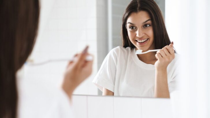 Family member brushing teeth in front of a mirror as part of a healthy daily oral care routine.