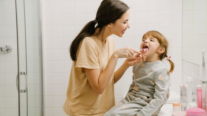 Parent assisting child with brushing teeth in bathroom.