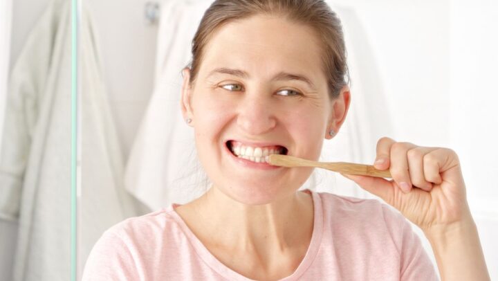 A woman brushes her teeth with a bamboo toothbrush, illustrating proper daily oral hygiene habits and common brushing mistakes.