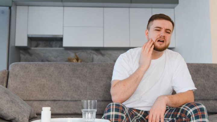 Man holding jaw in pain from toothache at home.