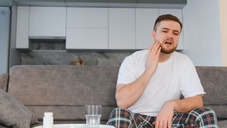 Man holding jaw in pain from toothache at home.